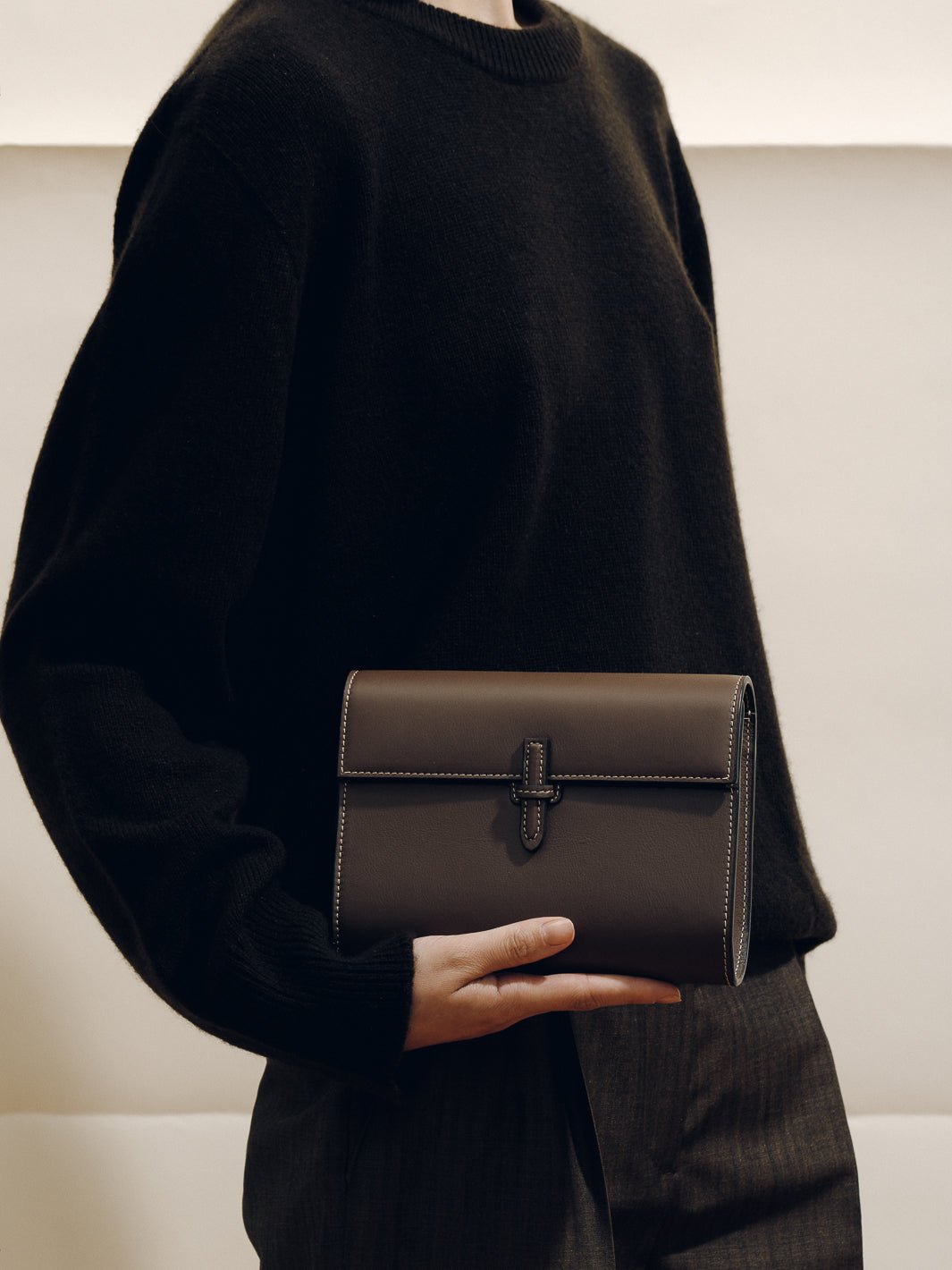 Front view of The Small Soft Clutch in Dark Brown Nappa showcasing its fold-over silhouette and slip-through closure against a black outfit