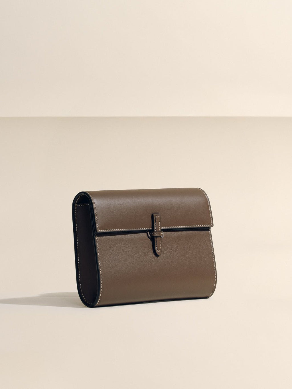 Front view of The Small Soft Clutch in Dark Brown Nappa showcasing its fold-over silhouette and slip-through closure on a light background