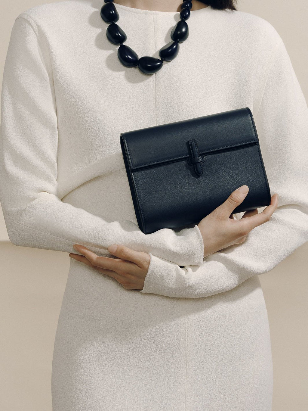 Front view of The Small Soft Clutch in navy nappa showcasing the fold-over silhouette and slip-through closure with a model in a white dress