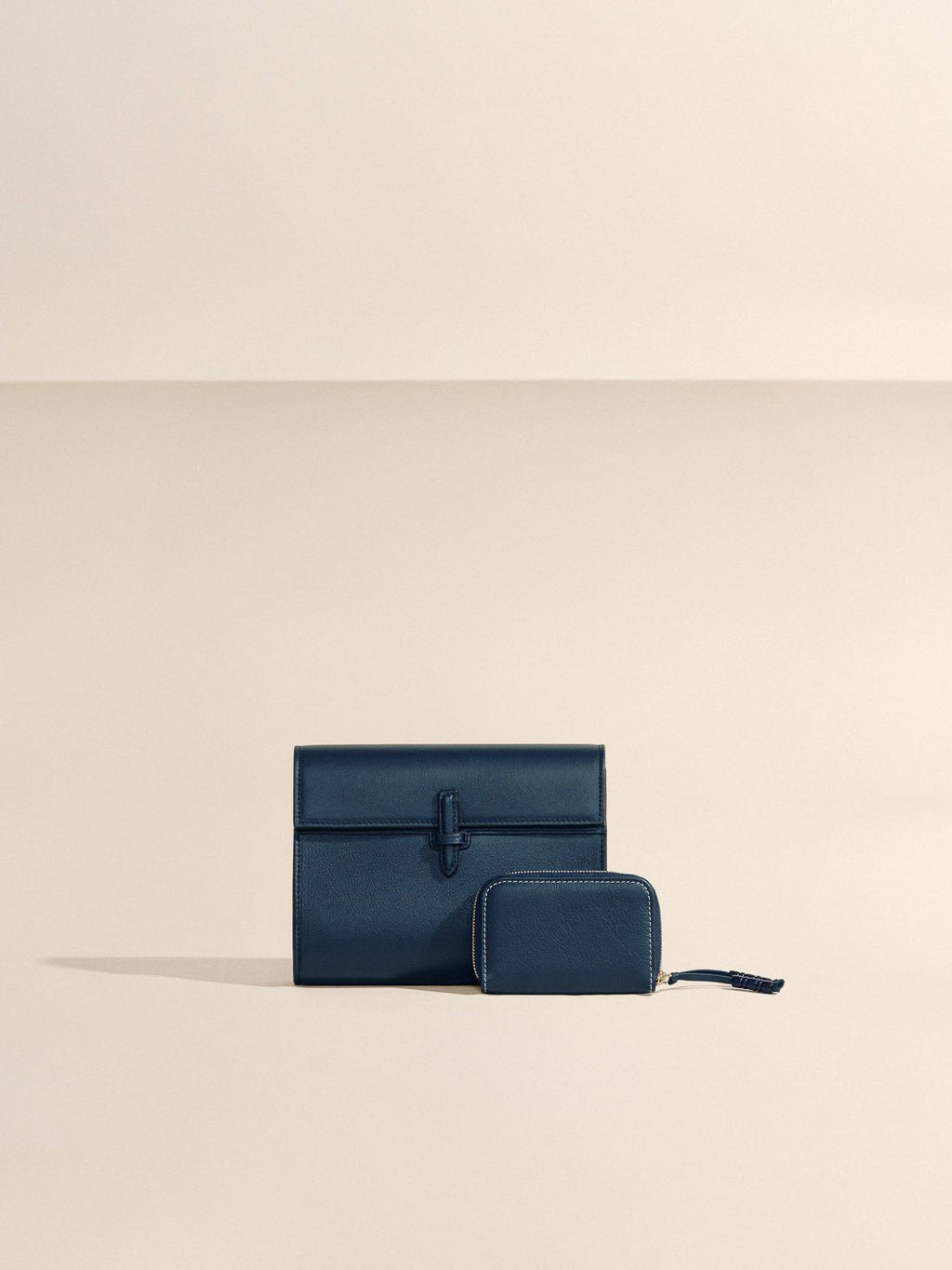 Front view of The Small Soft Clutch in navy Nappa leather showcasing its fold-over silhouette and slip-through closure against a beige background