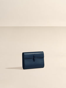 Front view of The Small Soft Clutch in Navy Nappa showcasing its fold-over silhouette and slip-through closure with a beige background