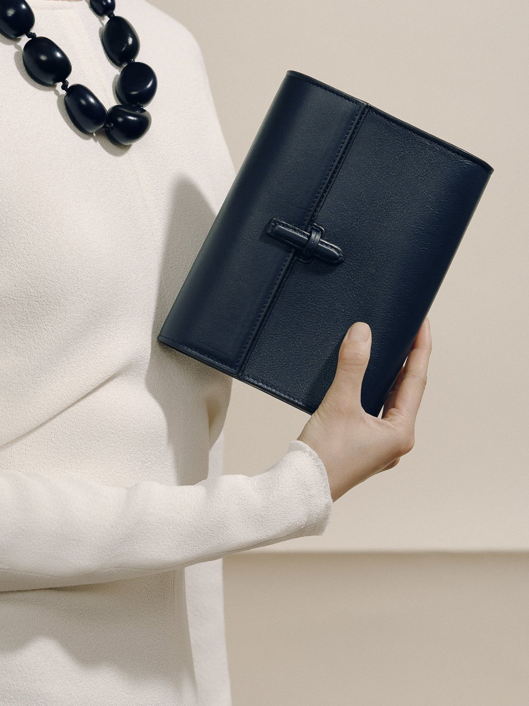 Front view of The Small Soft Clutch in Navy Nappa showcasing its slip-through closure while held against a neutral background