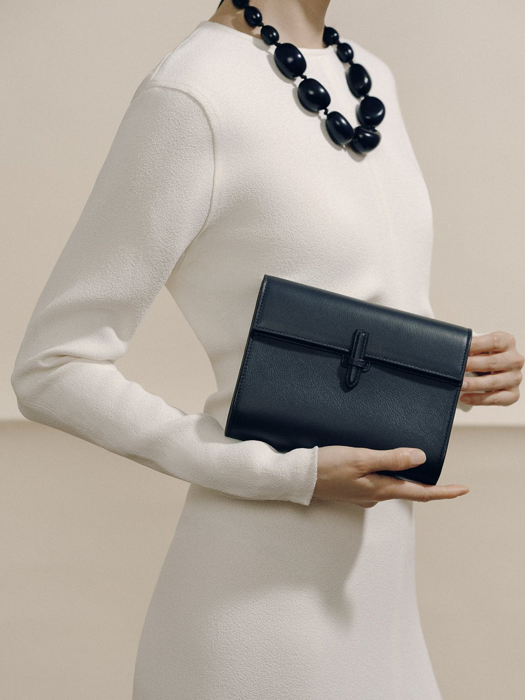 Front view of The Small Soft Clutch in Navy Nappa showcasing its slip-through closure, held by a model in white clothing