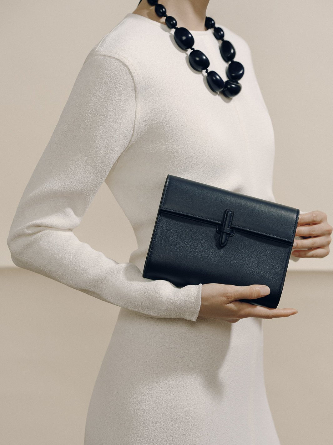 Front view of The Small Soft Clutch in Navy Nappa showcasing its slip-through closure, held by a model in white clothing