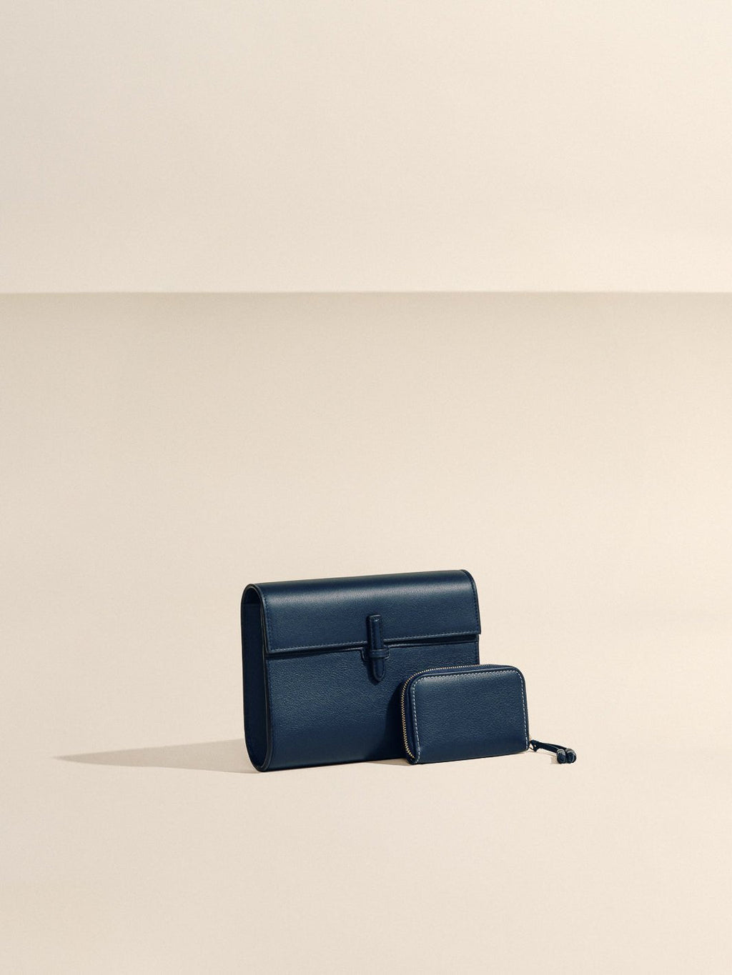 Front view of The Small Soft Clutch in Navy Nappa showcasing its fold-over silhouette and slip-through closure against a beige background