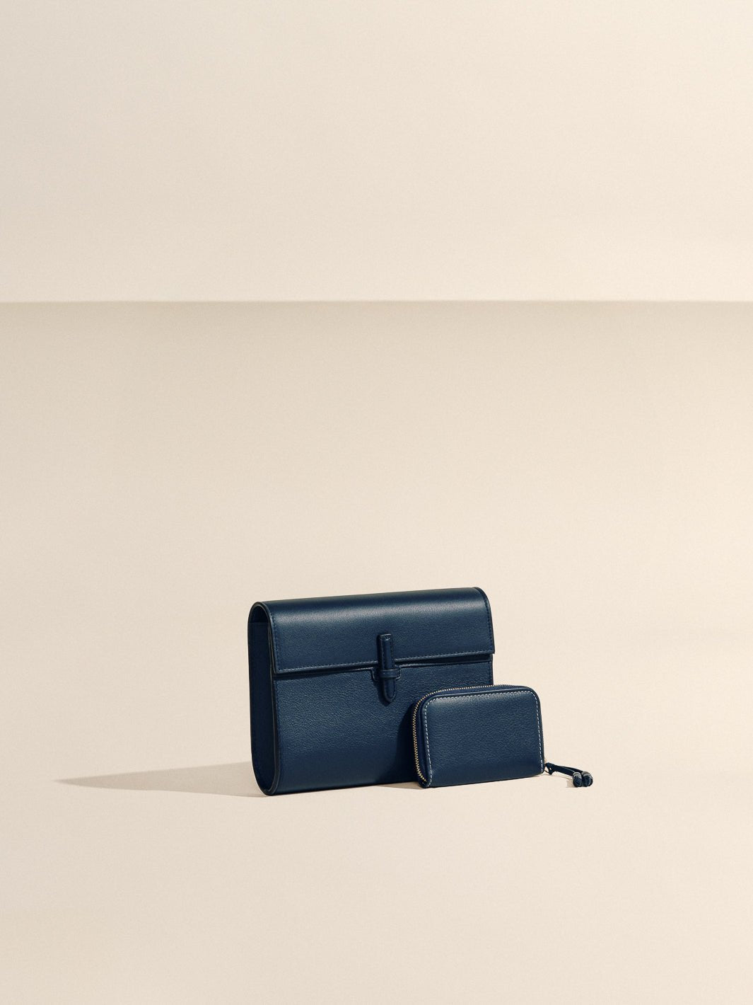 Front view of The Small Soft Clutch in Navy Nappa showcasing its fold-over silhouette and slip-through closure against a beige background