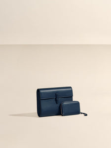 Front view of The Small Soft Clutch in Navy Nappa showcasing its fold-over silhouette and slip-through closure against a beige background