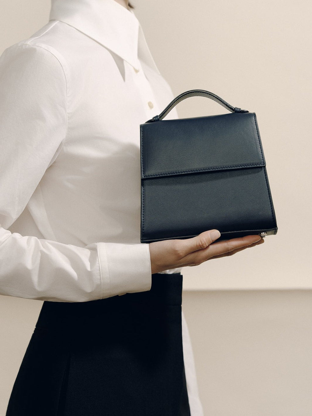 Front view of The Small Top Handle in navy Nappa leather showcasing its rounded handle held by a model