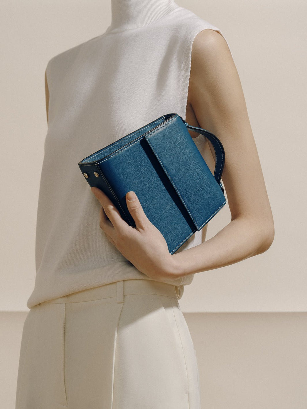 Three-quarter view of The Small Top Handle in Nappa teal showcasing rounded top handle, boxy silhouette, and white topstitching against a neutral studio background
