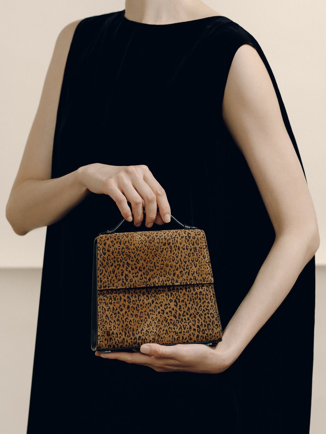 Front view of The Small Top Handle in animal print suede showcasing its structured silhouette and top handle on a model in a black dress