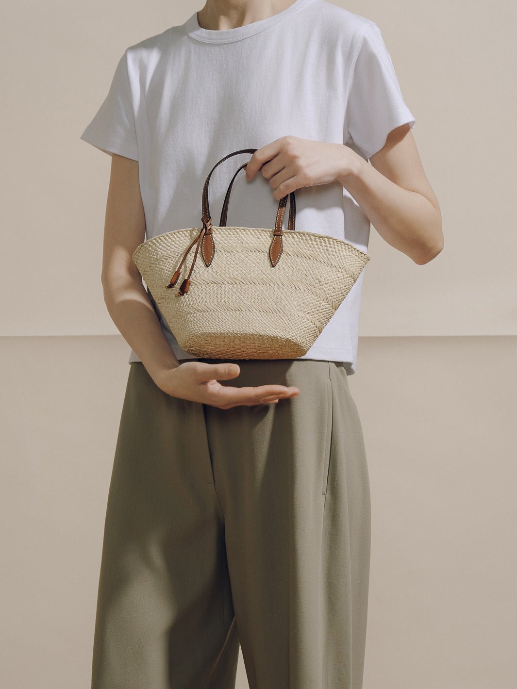Front view of The Small Trapeze Basket in natural cognac showing handwoven iraca body, cognac leather top handles and tie closure against a neutral background