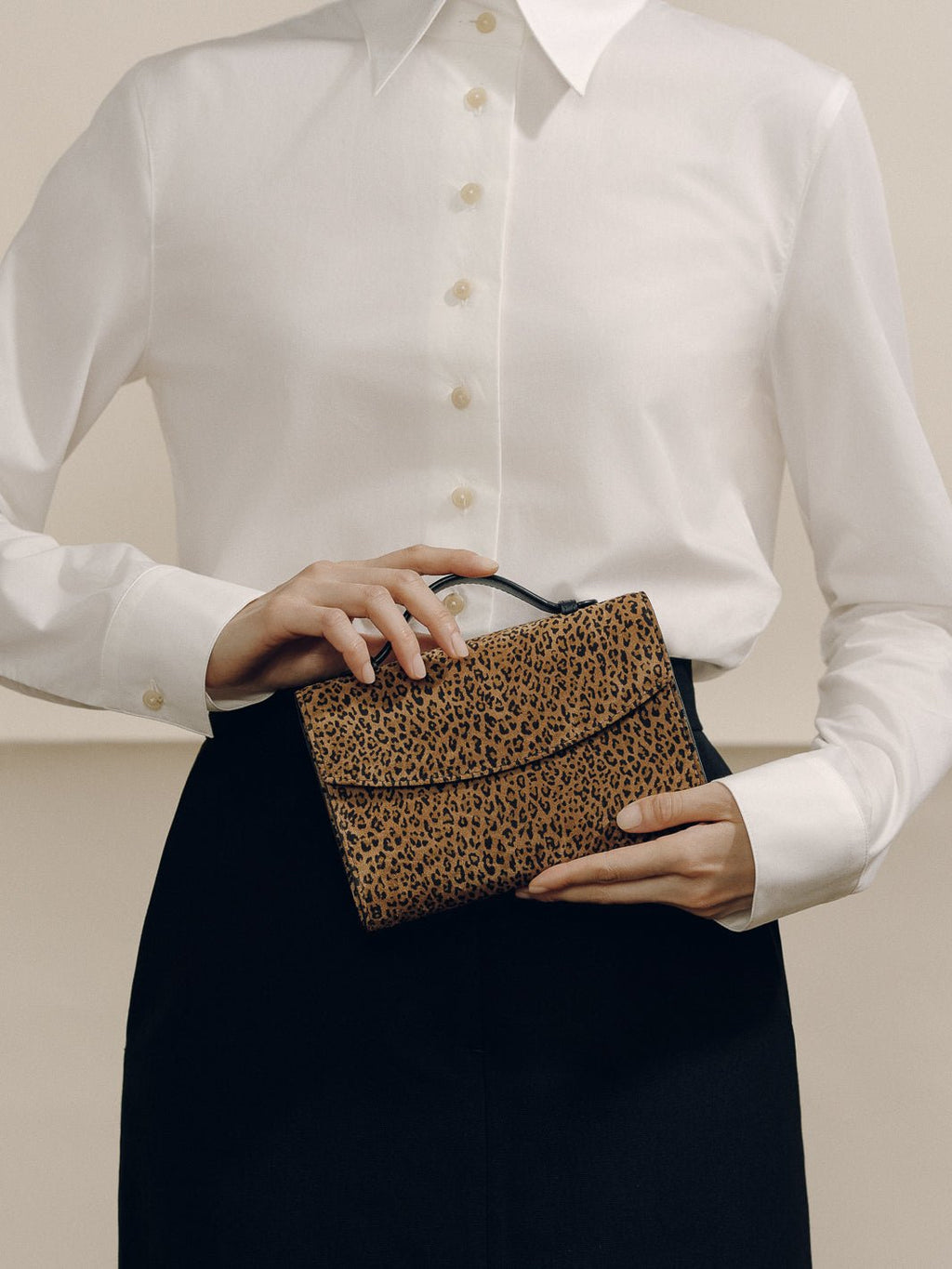 Front view of the animal print nappa leather top handle clutch showcasing its compact silhouette with a model in a white blouse and black skirt