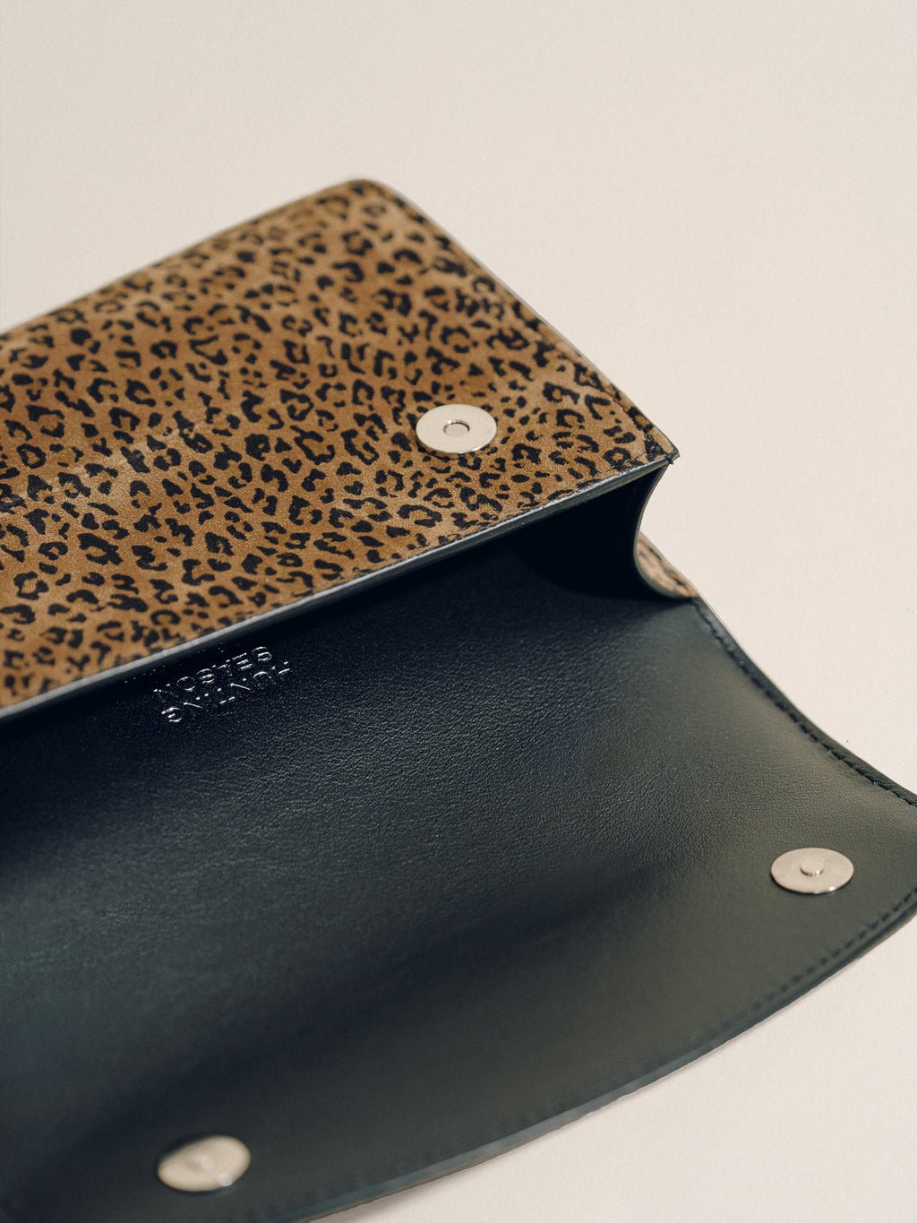 Open view of the Top Handle Clutch in Animal Print Nappa showcasing its dark interior and snap closures on a light background