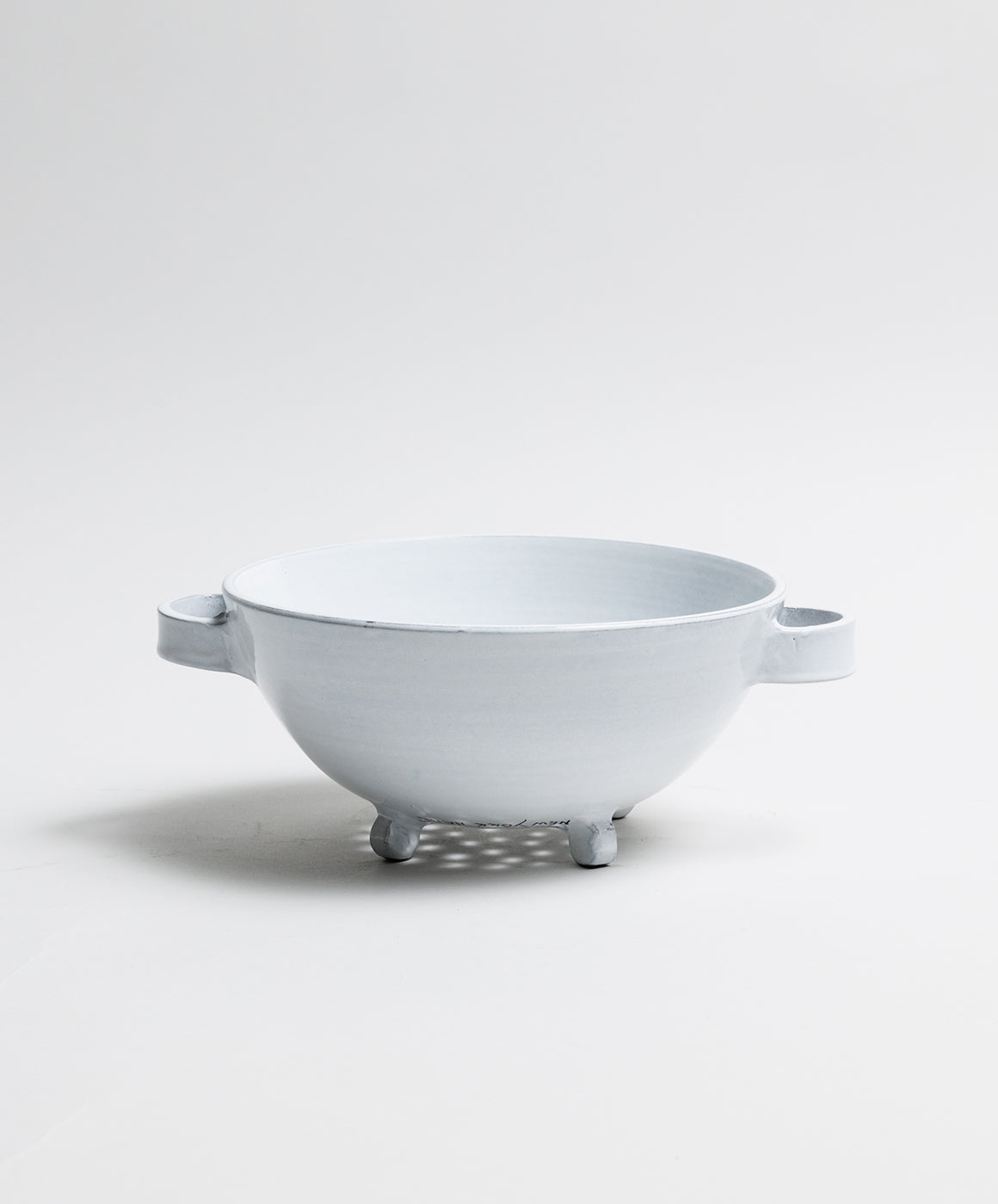 Side view of Assisi handled colander showcasing Bianco glaze, dual handles and three small feet on white background