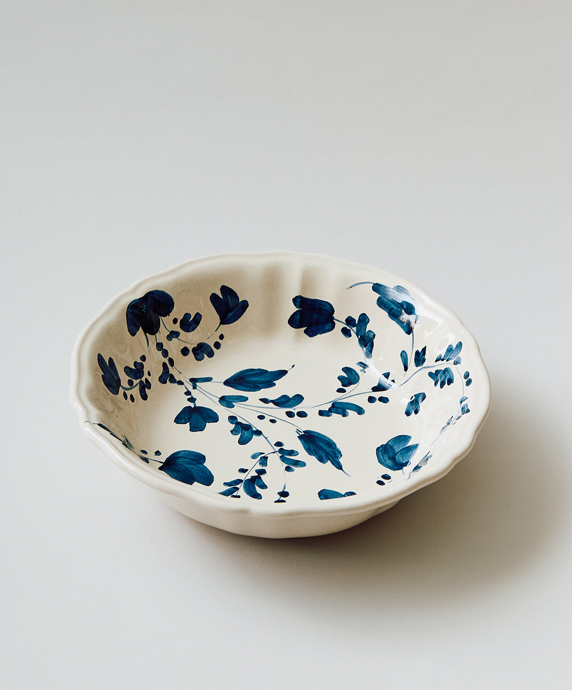 Angled top view of Flora small serving bowl with blue hand-painted floral motif and scalloped rim on light background