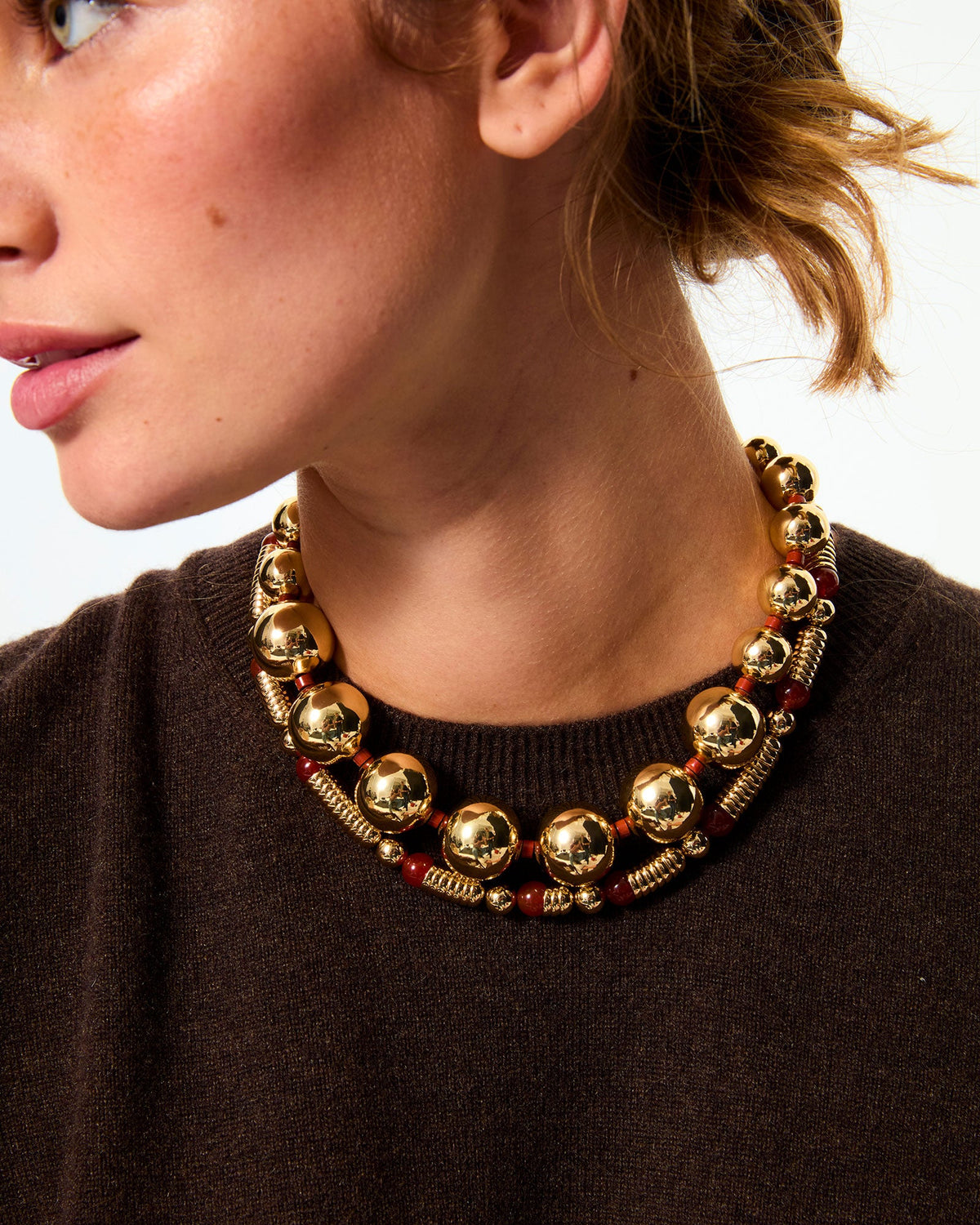 Close-up of The Very Big Bead Necklace in gold showcasing oversized polished gold-tone beads and red jasper spacer beads on a model’s neck