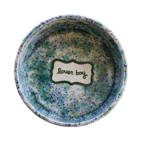 Top-down view of hand-painted ceramic dog bowl with green-blue speckled glaze and hand-painted “lover boy” label on white background