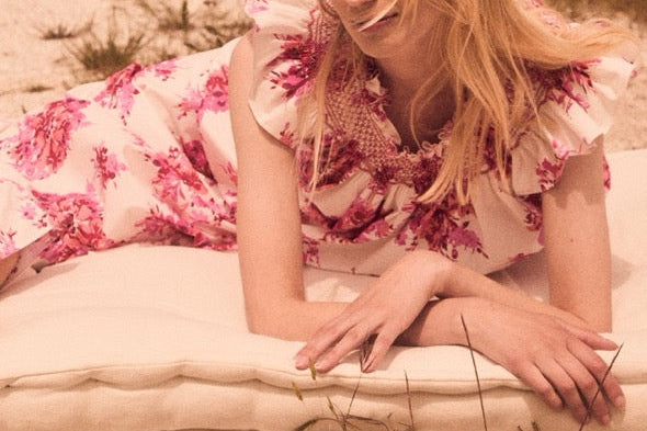 Reclining front view of Delfina Dress in Cloud Bouquet with ruffled collar and hand-embroidered smocking on cushion