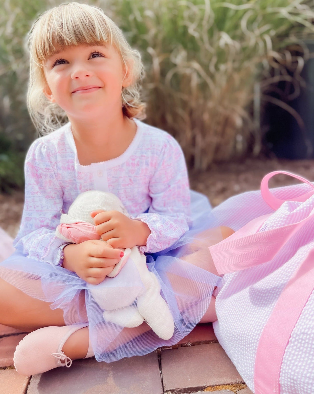 Front view of Ballet Girls Tess Lounge Dress showing pink hand-drawn ballet print on a child outdoors with stuffed bunny
