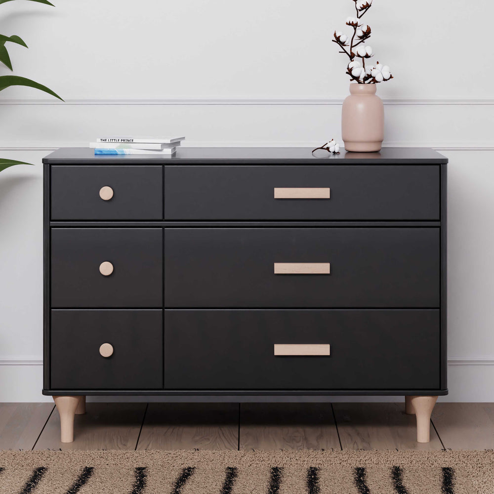 Front view of Lolly 6-drawer dresser in black with washed natural wood knobs, rectangular handles, and tapered legs, styled with vase and books