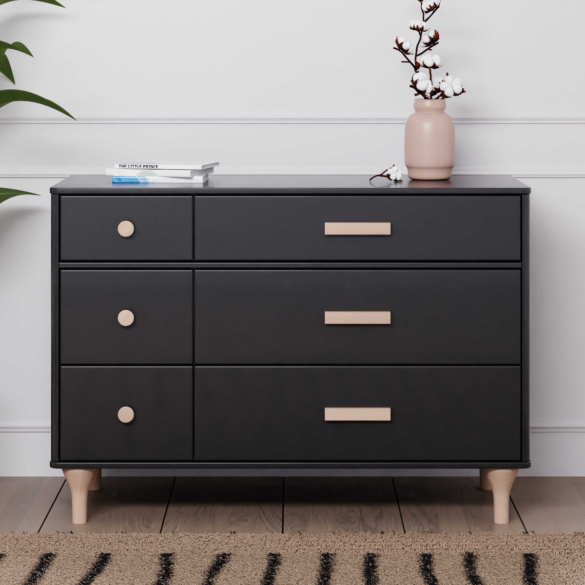Front view of Lolly 6-drawer dresser in black with washed natural wood knobs, rectangular handles, and tapered legs, styled with vase and books
