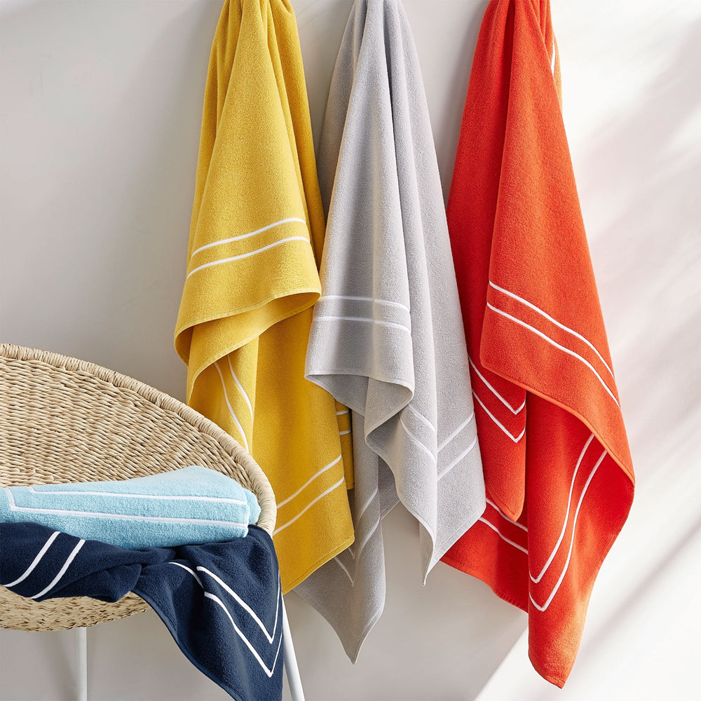 Three-quarter view of Amalfi Beach Towels showcasing double-embroidered borders in assorted colors hanging with a woven basket