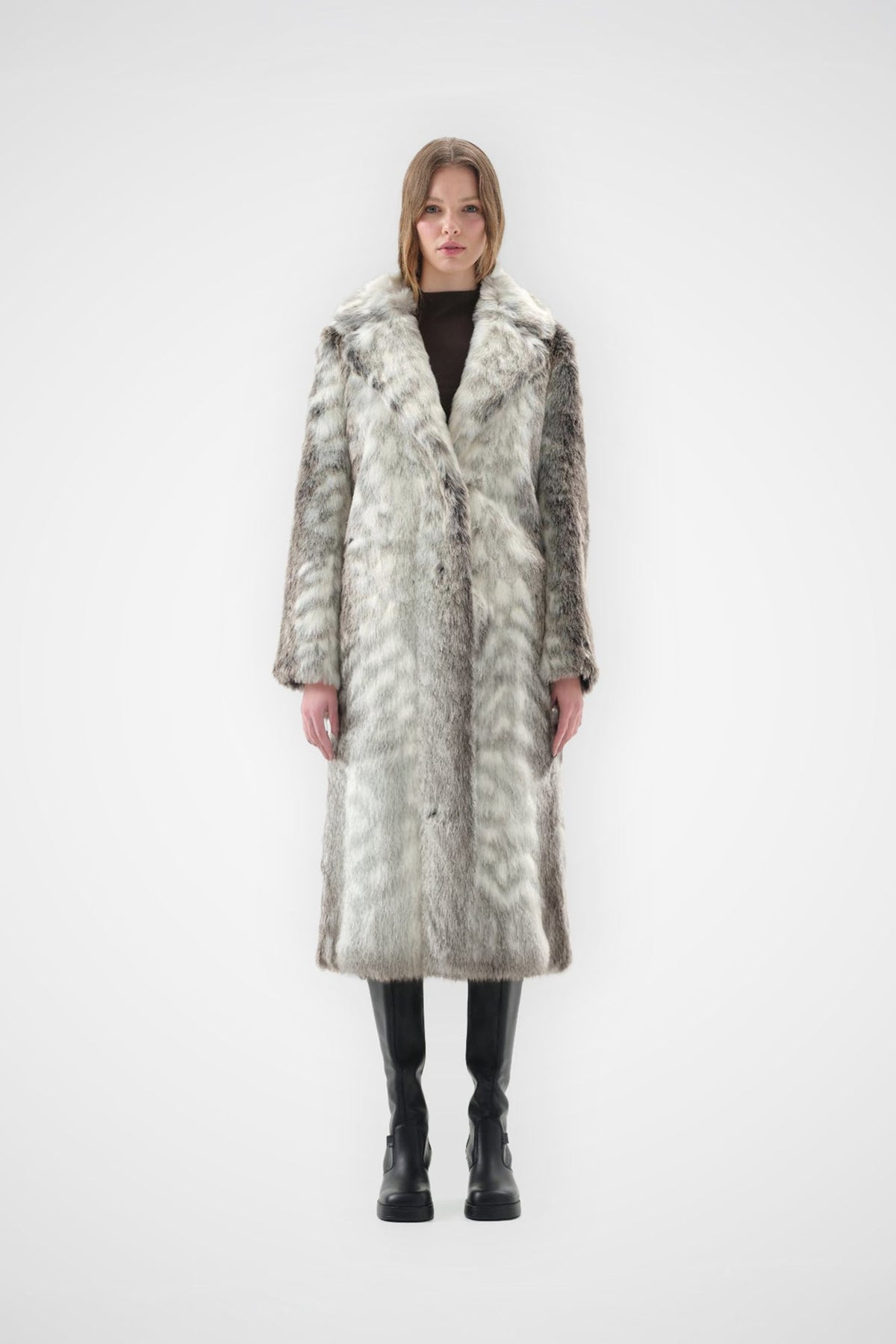 Grey and cream snow leopard faux fur coat with notch lapel and full-length, relaxed fit, worn over black knee-high boots, front view
