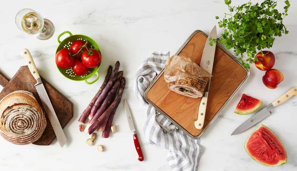 Top-down view of cherry wood cheese tray with pewter handles showcasing removable cherry wood insert on a marble tabletop with bread, asparagus, and fruit