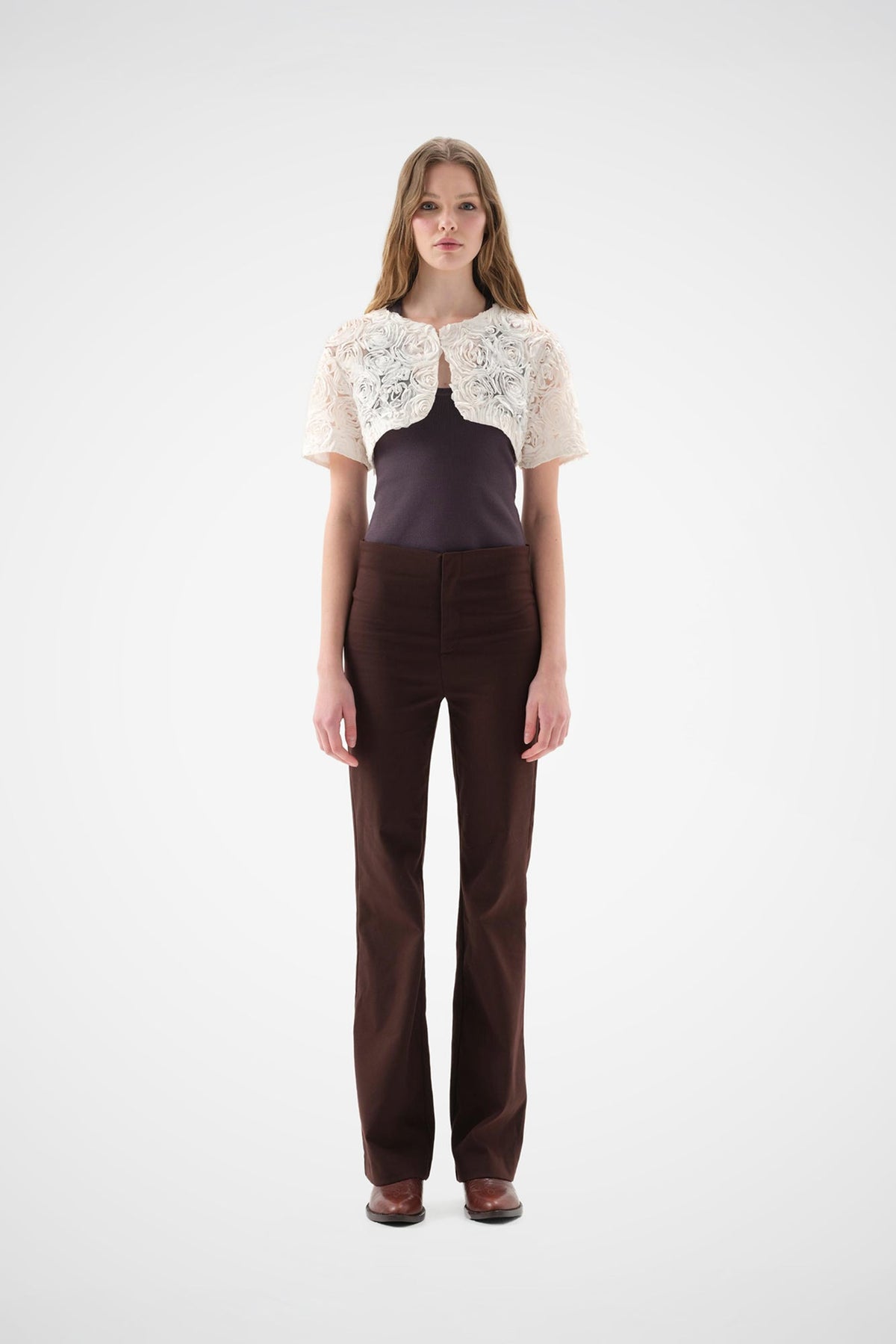Cream lace bolero with floral rose embroidery, short-sleeve cropped fit, worn over a dark top and brown trousers.