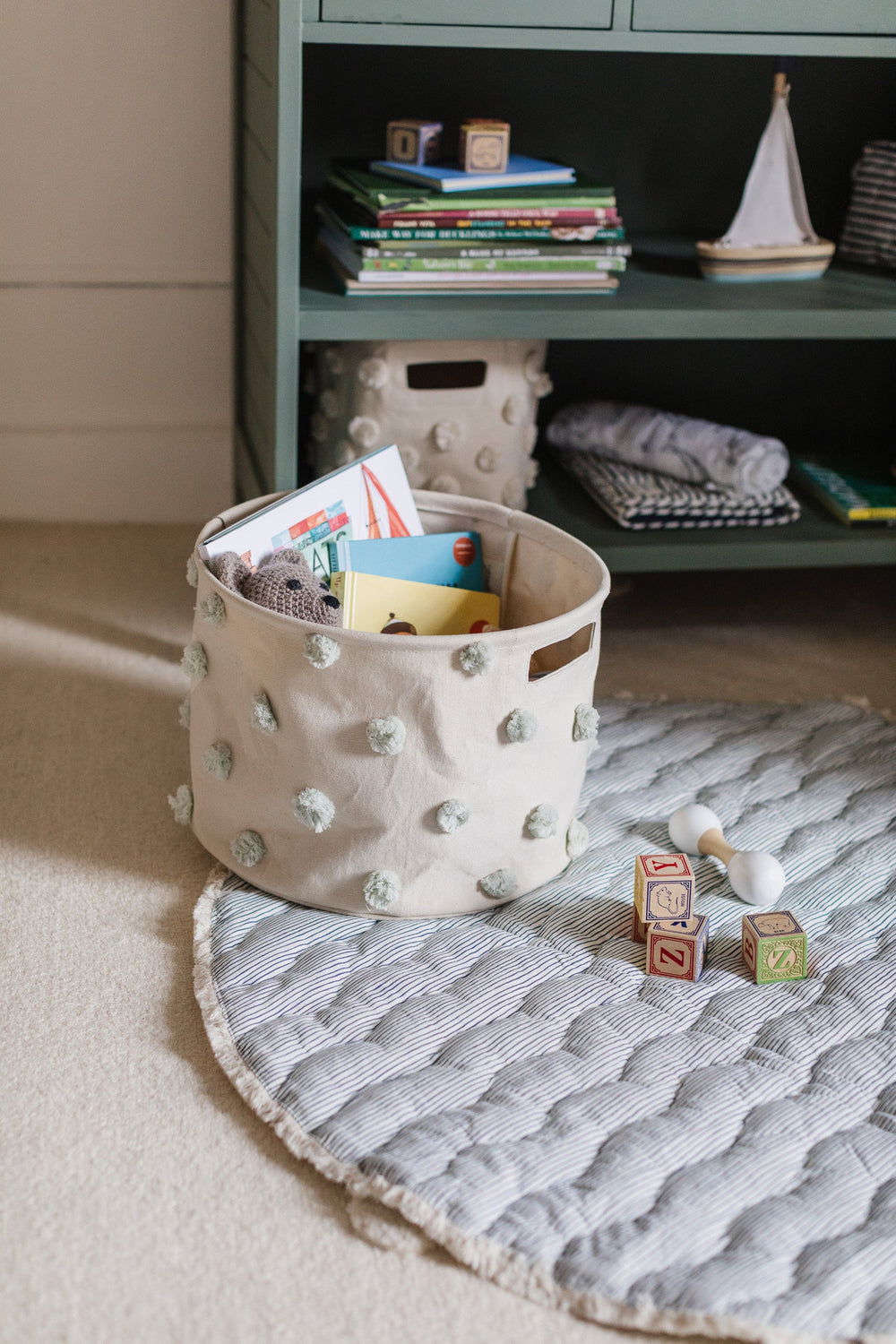 Angled view of Life Aquatic baby play mat showcasing quilted striped surface and round shape on nursery floor with toy basket and wooden blocks