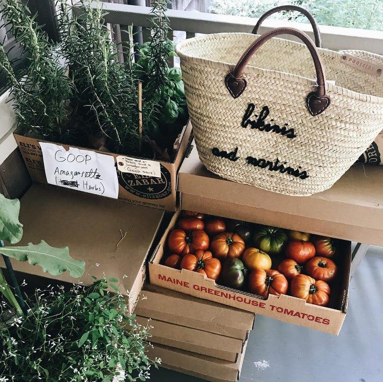 Front view of large straw beach tote with leather handles showing hand-embroidered bikinis and martinis on produce boxes