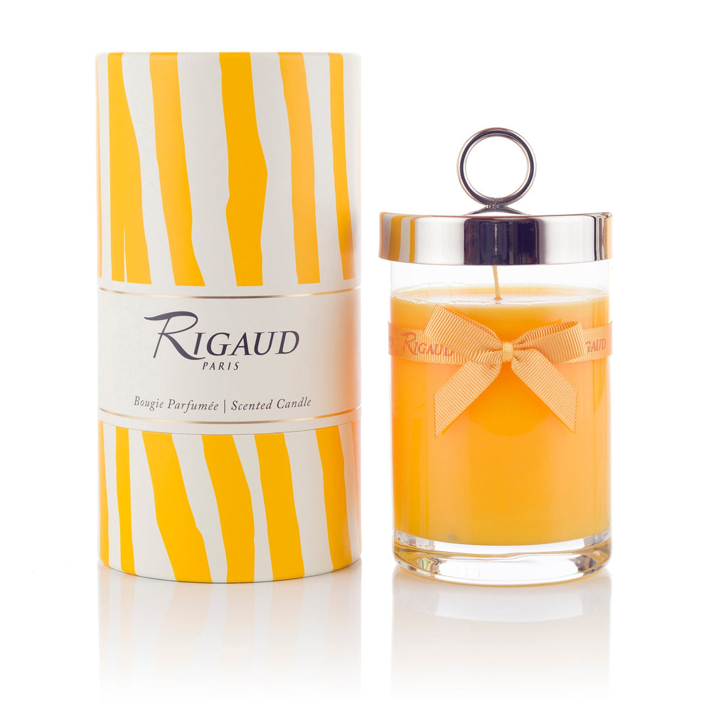 Front view of Rigaud Tournesol scented candle in glass jar with silver loop lid and ribbon beside yellow-striped tube box on white background