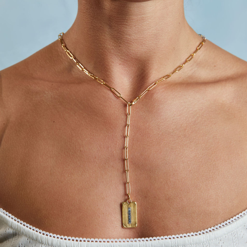 Close up of Long Link Lariat Starter Necklace showcasing gold link chain and rectangular pendant with blue stones on model