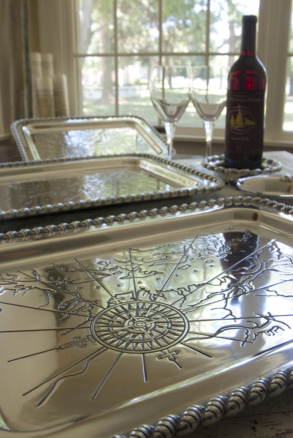 Close-up of Latitudes Medium Chesapeake tray showcasing embossed compass map with wine bottle and glasses near window