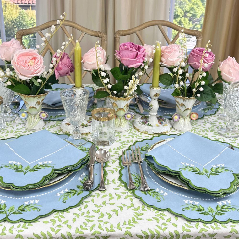 table setting with floral centerpieces, plates, and cutlery on a patterned tablecloth. Luxury Lilly of the valley embroidered placemats and napkins