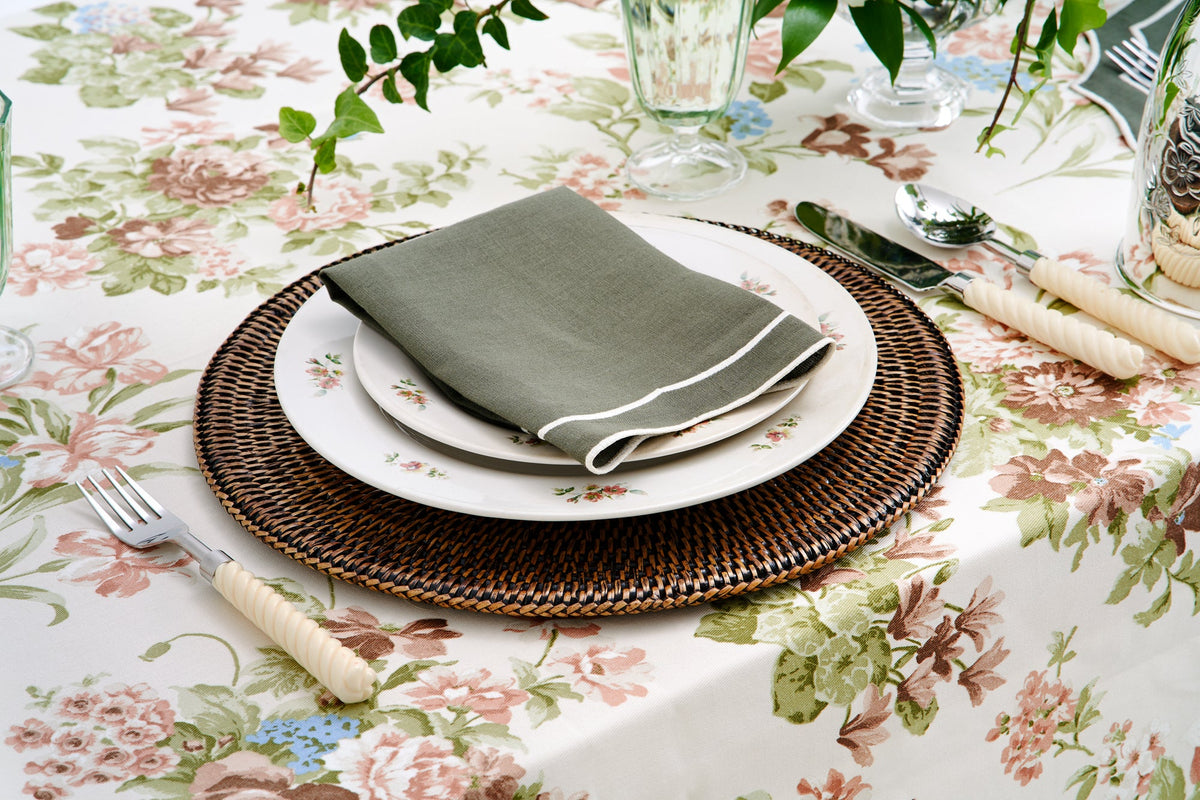 Angled view of Rattan Placemat showcasing round woven natural rattan in an earth tone with a floral table setting