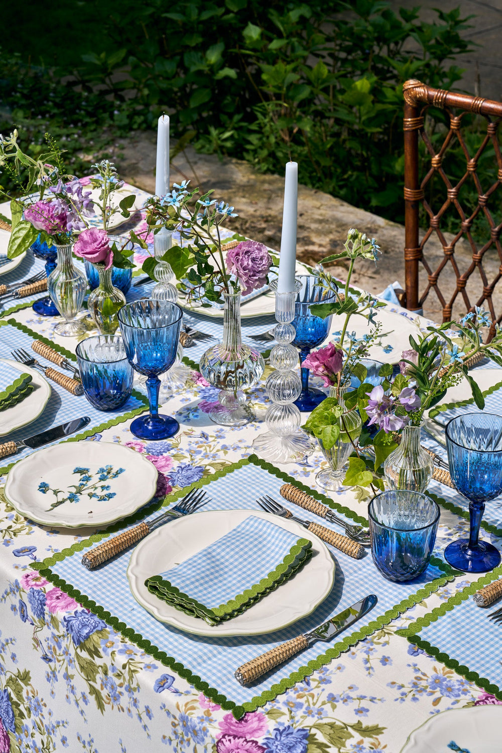 Angled view of Maisie napkins (set of 4) showing blue gingham pattern with green scalloped trim on a floral tablecloth with blue glassware