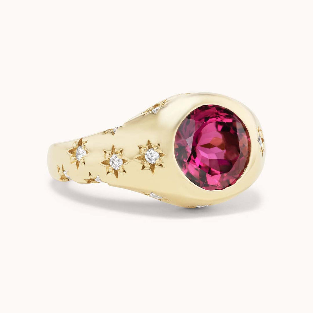 Angled view of Disco Ring with round pink tourmaline center and carved star motifs set with small diamonds on a pale background