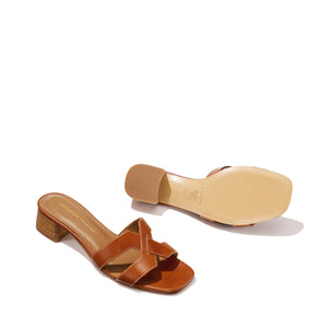 A pair of Margaux-development’s The MX 35 - Saddle Calf block-heeled sandals with crisscross leather straps is shown: one upright revealing the top and heel, the other on its side to display the sole, against a plain light background.