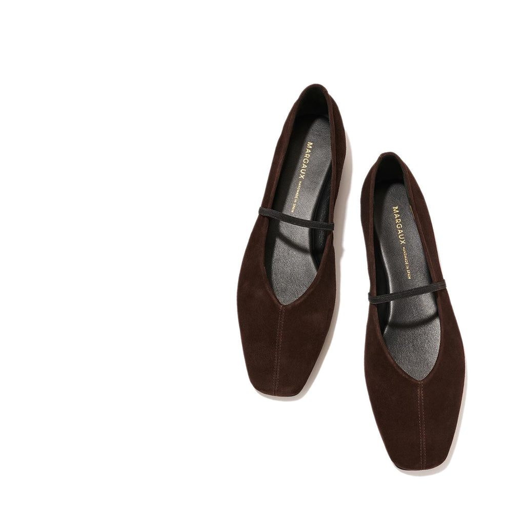 The Phoebe - Espresso Suede by margaux-development: dark brown suede flats with black soles and a slim black strap, sacchetto construction for comfort and flexibility, shown on a light beige background.