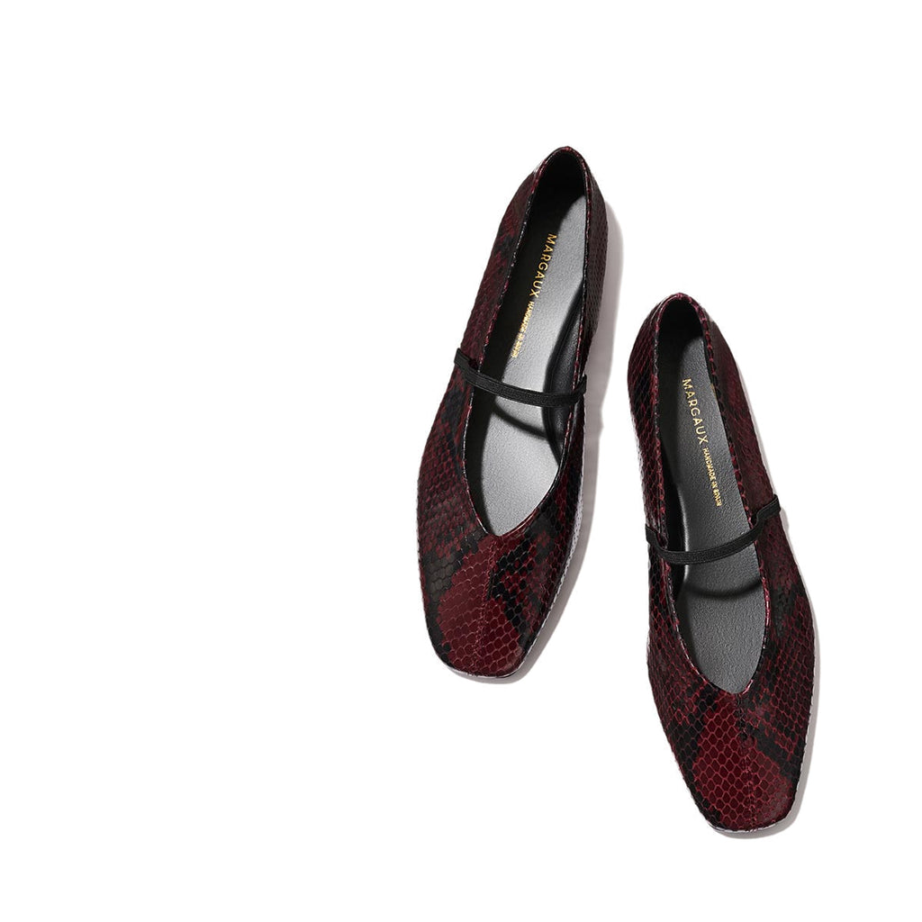 The Phoebe - Burgundy Python Embossed by margaux-development: burgundy and black snakeskin-patterned Mary Jane flats with a single black strap, sacchetto construction for plush comfort, shown on a light beige background.