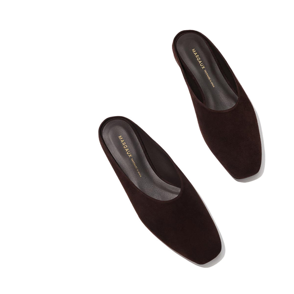 The Clara - Espresso Suede by Margaux: dark brown suede slip-on mules with a square toe and slipper-like silhouette, shown on a light beige background. Black insoles feature gold "Margaux New York" text.