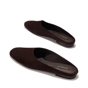The Clara - Espresso Suede by Margaux are dark brown suede slip-on mules with flat soles and a minimalist, slipper-inspired design. Shown on a light background, the brand name Margaux is visible inside the shoes.
