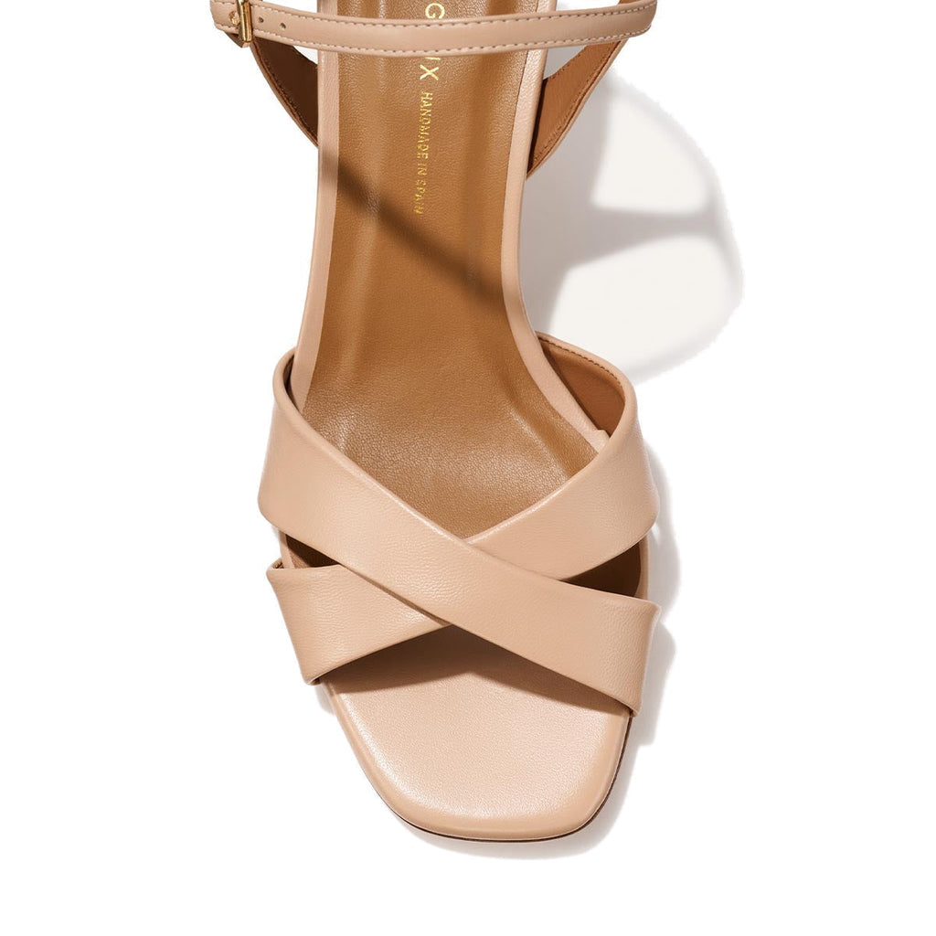 A close-up top view of Margaux’s The Paloma Sandal in Dune Nappa, featuring beige crisscross straps and a square-shaped open toe design against a light background.