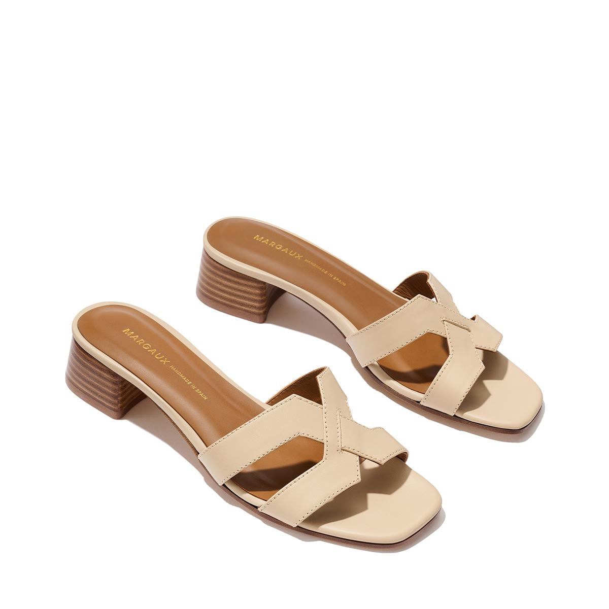A pair of Margaux’s The MX 35 - Latte Calf heeled sandals, featuring criss-cross straps and mid-height wooden block heels, shown in beige on a light background.