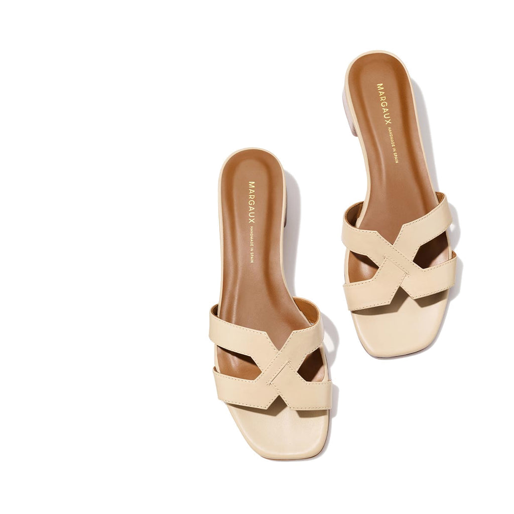 The MX 35 - Latte Calf by Margaux: beige slip-on sandals with crisscross straps, tan footbed, comfortable block heel, and square toe. MARGAUX branding on the insole; displayed on a light background.