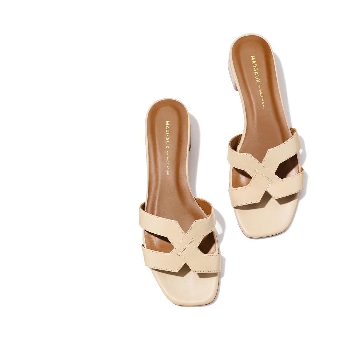 The MX 35 - Latte Calf by Margaux: beige slip-on sandals with crisscross straps, tan footbed, comfortable block heel, and square toe. MARGAUX branding on the insole; displayed on a light background.