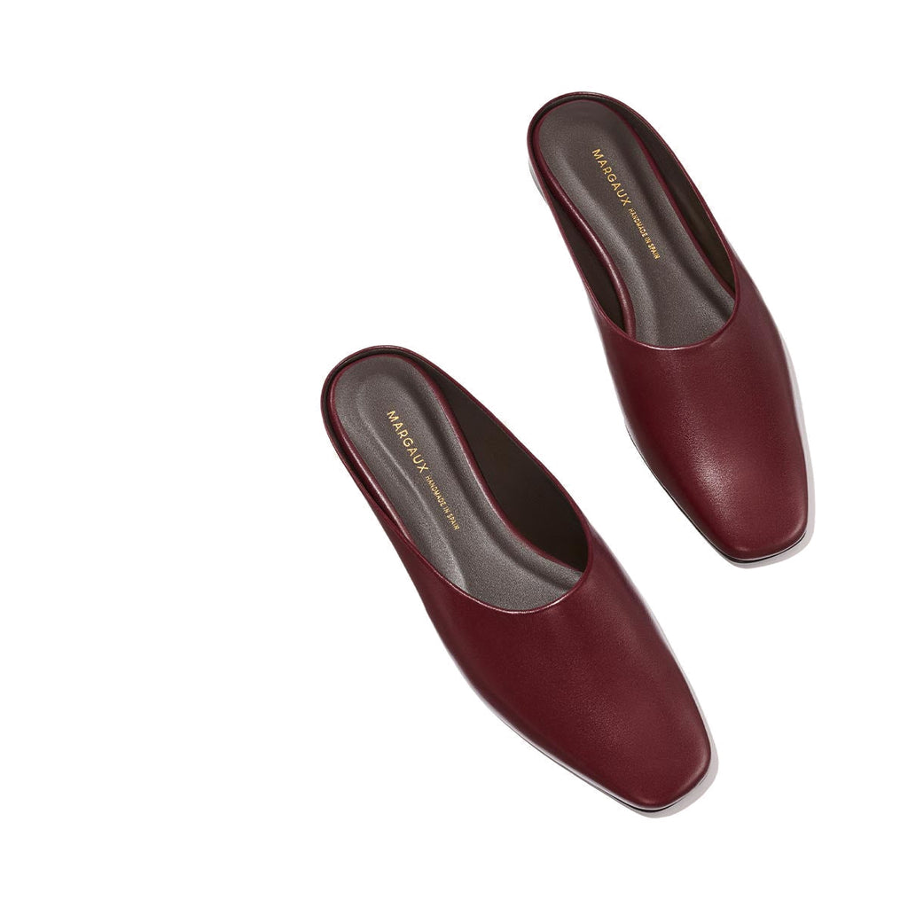 A pair of The Clara - Wine Calf slip-on mules by Margaux, featuring a square toe and versatile style, are displayed on a plain light background. The shoes have dark insoles with gold branding and appear new and unworn.