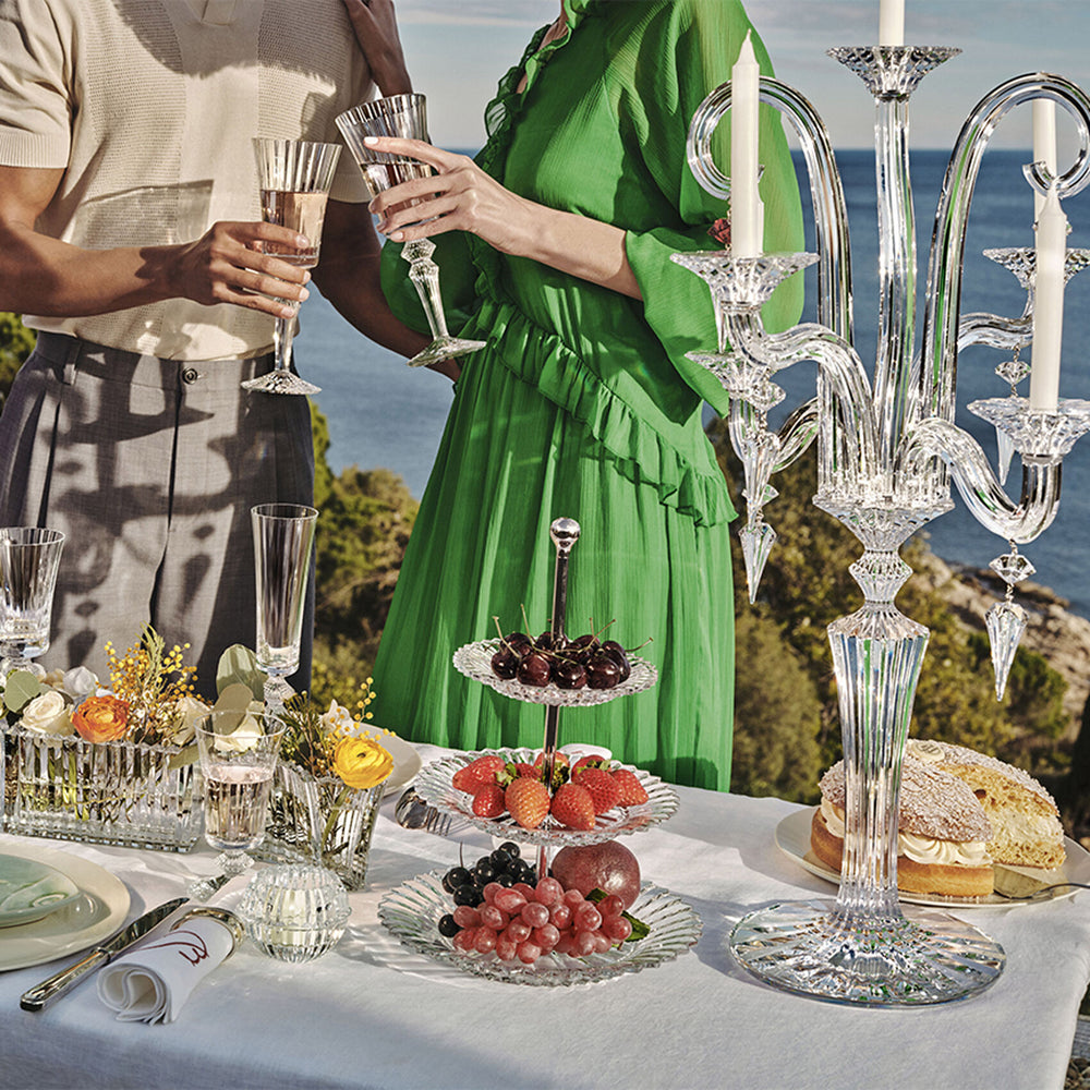 Couple toasting beside three-tier Mille Nuits crystal pastry stand with fruit on seaside table setting