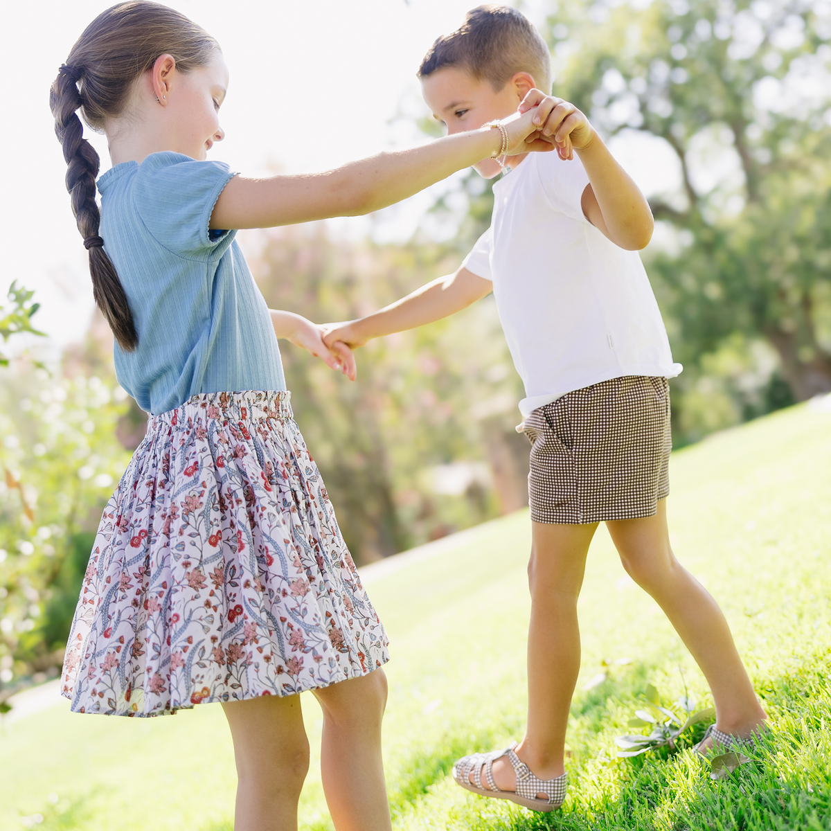 Girl twirling in a white floral Mercado Bloom skirt with elasticized waist, holding hands with a boy in a sunlit park